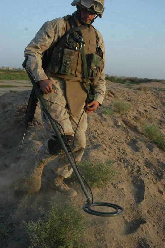 AR RAMADI, Iraq (Aug. 15, 2005) - Corporal Nicklas E. Schmitter, a combat engineer with 4th Platoon, Company A, 1st Combat Engineer Battalion, which is in direct support of 1st Battalion, 5th Marine Regiment, trudges through a field in search of buried weapons during a cache sweep through farmland on the outskirts of the city here Aug. 15. The 21-year-old from Stockport, Iowa, and other Marines with 4th Platoon found more than 300 artillery shells and approximately 2000 rounds of 7.62 mm ammunition during the mission. They consolidated the munitions into one whole and destroyed them with plastic explosives. Photo by: Cpl. Tom Sloan