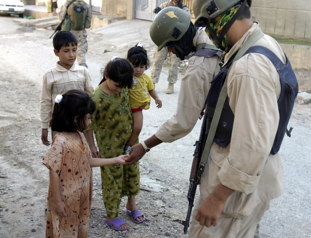 FALLUJAH, Iraq - Iraqi policemen with the Public Order Brigade hand candy out to several local children while patrolling the streets besides U.S. Marines here Sept. 15 during Operation Hard Knock.  ISF and Marine personnel detained three suspected insurgent supporters and confiscated one hand grenade during this three-hour-long house-to-house search mission.