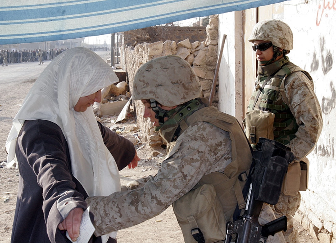19-year-old Escanaba, Mich., native Lance Cpl. Amber J. Anderson searches an Iraqi woman December 15 in the Iraqi city of Husaybah prior to being allowed entrance to a polling station while Lance Cpl. Gabriela Altamira provides security. Islamic culture requires that Muslim women be searched only by women. The vote today is being held in order to elect a permanent Iraqi government.