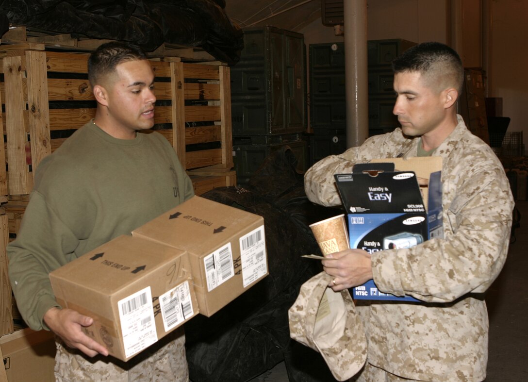 MARINE CORPS BASE CAMP LEJEUNE, N.C. - Lance Cpl. Miguel A. Suarez, left, 1st Battalion, 6th Marine Regiment supply warehouse clerk, distributes boxes of gear to a fellow Marine at the unit's supply warehouse.  The Tampa, Fla. native helps oversee the acquisition and distribution of items 1st Battalion, 6th Marine Regiment Marines will need for their deployment to Iraq in March, such as desert camouflage utility uniforms and ballistic eyewear.