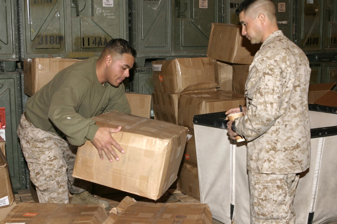 MARINE CORPS BASE CAMP LEJEUNE, N.C. - Lance Cpl. Miguel A. Suarez, left, 1st Battalion, 6th Marine Regiment supply warehouse clerk, stacks boxes of gear as he prepares to distribute them to a fellow Marine.  The Tampa, Fla. native helps oversee the acquisition and distribution of items 1st Battalion, 6th Marine Regiment Marines will need for their deployment to Iraq in March, such as desert camouflage utility uniforms and ballistic eyewear.