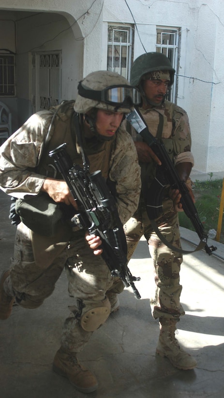 AR RAMADI, Iraq (May 16, 2005) - Lance Cpl. Anthony J. Diklich, a squad automatic machine gunner with 2nd Squad, 3rd Platoon, Company A, 1st Battalion, 5th Marine Regiment, and a New Iraqi Army (NIA) soldier charge out off the entrance of a residence here after searching it during a mission. The 23-year-old from Roy, Wash., and his fellow warriors with 3rd Platoon conducted a cordon and search mission of a neighborhood with 15 NIA soldiers. The three-hour joint-operation was geared toward keeping a military presence in area and establishing a positive relationship between Iraqi civilians and members of their own military. The Marines and their Iraqi counterparts executed the mission without incident. Photo by: Cpl. Tom Sloan