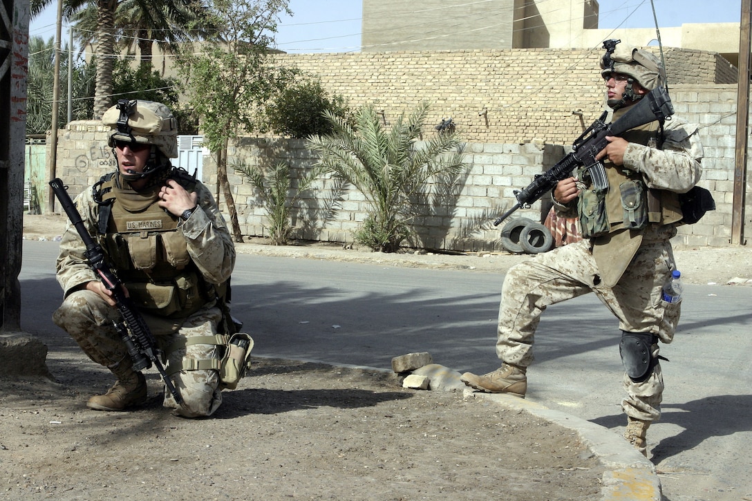FALLUJAH, Iraq - Second Lieutenant Joseph Davis, 3rd Platoon commander, Company C, 1st Battalion, 6th Marine Regiment, talks on the radio while his radio operator, Lance Cpl. Brandon Sunderlin, provides security along a city street July 16 during Operation Hard Knock.  Company C personnel worked alongside other battalion infantrymen and Iraqi Security Forces to search through a wired-off sector of Fallujah for weapons and insurgent activity, as well as gather census information on the populace.