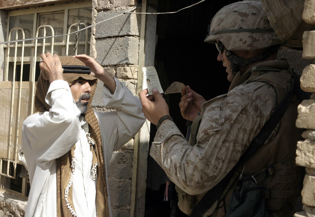 FALLUJAH, Iraq - Lance Cpl. John Tracz, an infantryman with 2nd Squad, 3rd Platoon, Company C, 1st Battalion, 6th Marine Regiment, checks a local man's identification card here July 16 during Operation Hard Knock.  Company C personnel worked alongside other battalion infantrymen and Iraqi Security Forces to search through a wired-off sector of Fallujah for weapons and insurgent activity, as well as gather census information on the populace.