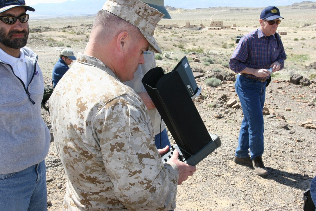 Colonel James Braden, Chief of Staff, Marine Corps Air Ground Combat Center, controls the Wasp micro-air vehicle with the ground control unit?s control pad as Dr. Leo Christodoulou, Wasp program manager, Defense Research Advanced Projects Agency watches. The Combat Center?s new military operations in urban terrain facility is in the background.