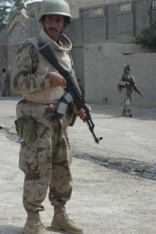AR RAMADI, Iraq (April 17, 2005) - A member of the Iraqi Intervention Forces posts security from a street corner during a patrol through the city here. A Marine with 3rd Platoon, Company C, 1st Battalion, 5th Marine Regiment, trails close behind and backs him up. Fifteen IIF members accompanied Marines with 3rd Platoon, Company C, 1st Battalion, 5th Marines, and, together, conducted a combat patrol. The three-hour joint-mission was geared towards fine-tuning the IIF members' patrolling techniques by providing them with hands-on training in a combat environment. Marines with 3rd Platoon, Company C, 1st Battalion, 5th Marines, showed their IIF counterparts proper dispersion, how to post security and set up over watches and other patrolling fundamentals. In the not so distant future, the IIF assume full responsibility of conducting security and stabilization operations when they are competent enough to successfully patrol the city on their own.  Photo by Cpl. Tom Sloan