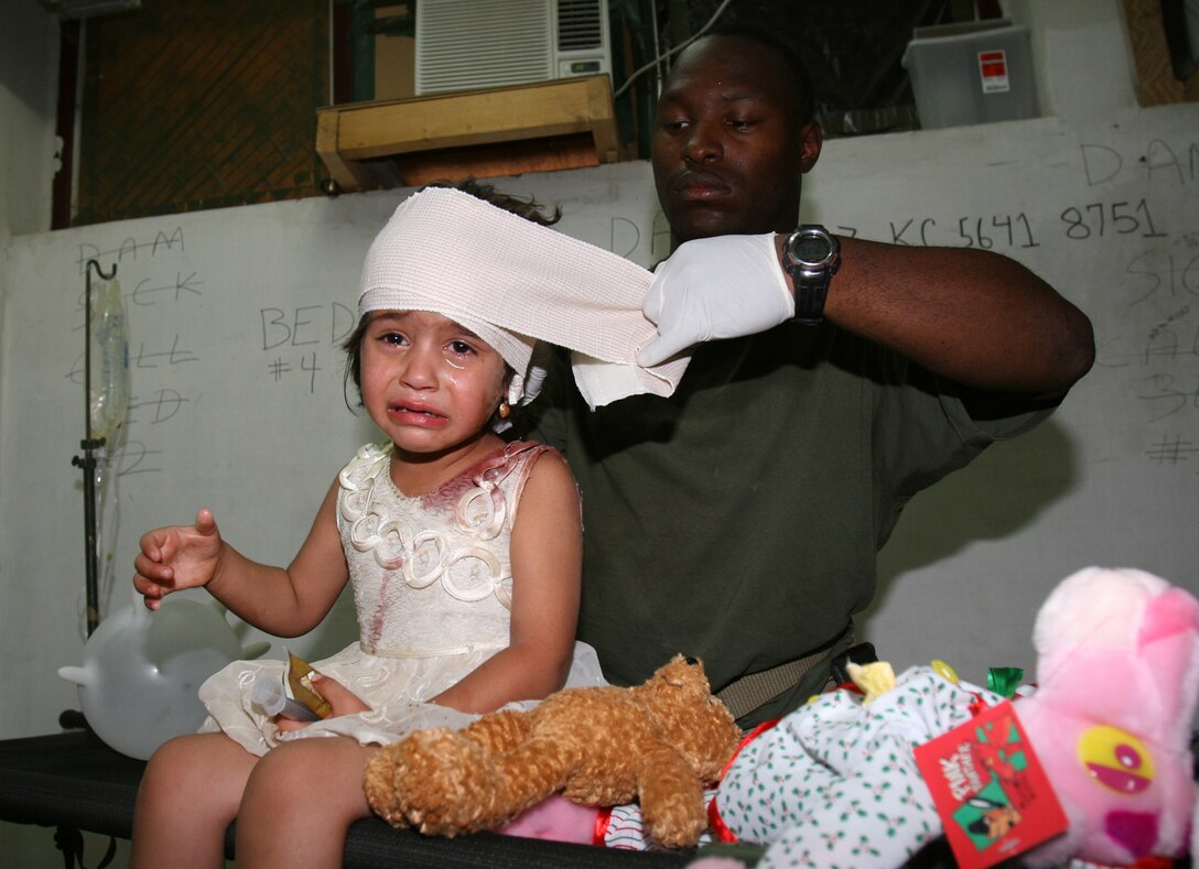 Camp Hadithah Dam, Hadithah, Al Anbar (June 17,2005) -- Hospitalman Robert D. Bush loosens the bandage on an injured Iraqi girl's head.  The 3rd Battalion, 25th Marines Battalion Aid Station is equipped to handle routine sick call to combat trauma injuries.  The corpsmen are on call 24 hours-a-day for treating the injured.