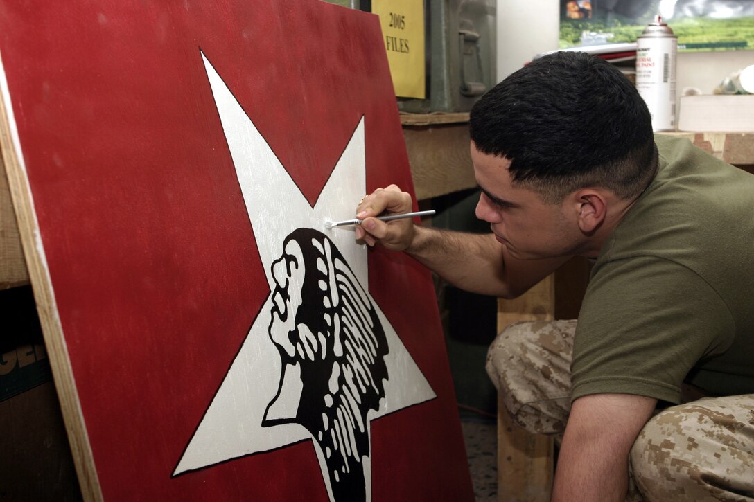 CAMP BAHARIA, Iraq - Lance Cpl. Luis Bonilla, an administration clerk with 1st Battalion, 6th Marine Regiment, puts the finishing touches on an 'Indian head' sign he created July 31 for display at the chapel here.  The 21-year-old Browns Mills, N.J. native helps resolve his fellow Marines' pay and promotion issues, and enjoys creating character sketches and painting during his free time.
