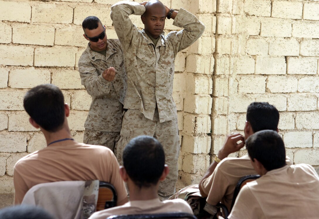 FALLUJAH, Iraq - Sgt. Jose Martins, chief instructor for 1st Battalion, 6th Marine Regiment's Iraqi Security Forces training cadre, frisks fellow instructor, Pfc. Philip Pepper, as he demonstrates proper personnel searching procedures to Iraqi soldiers during a combat leaders course here.  The 26-year-old Queens Village, N.Y. native and his seven teammates school dozens of Iraqi soldiers and policemen every month on topics such as first aid in combat, urban war fighting tactics, and weapons handling skills.