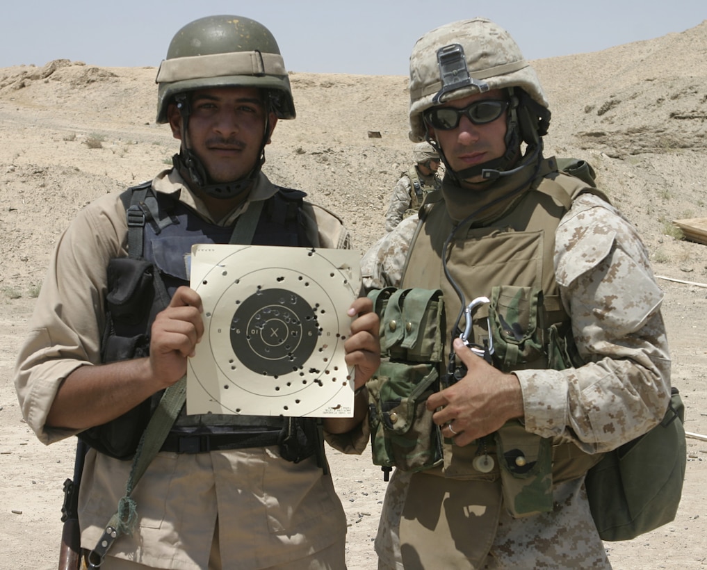 FALLUJAH, Iraq - Cpl. Brandon Connelly, an instructor with 1st Battalion, 6th Marine Regiment's Iraqi Security Forces training cadre, poses with an Iraqi policeman showing his target off after firing a training range here Aug. 3.  The 28-year-old Toms River, N.J. native and his seven teammates school dozens of Iraqi soldiers and policemen every month on topics such as first aid in combat, urban war fighting tactics, and weapons handling skills.