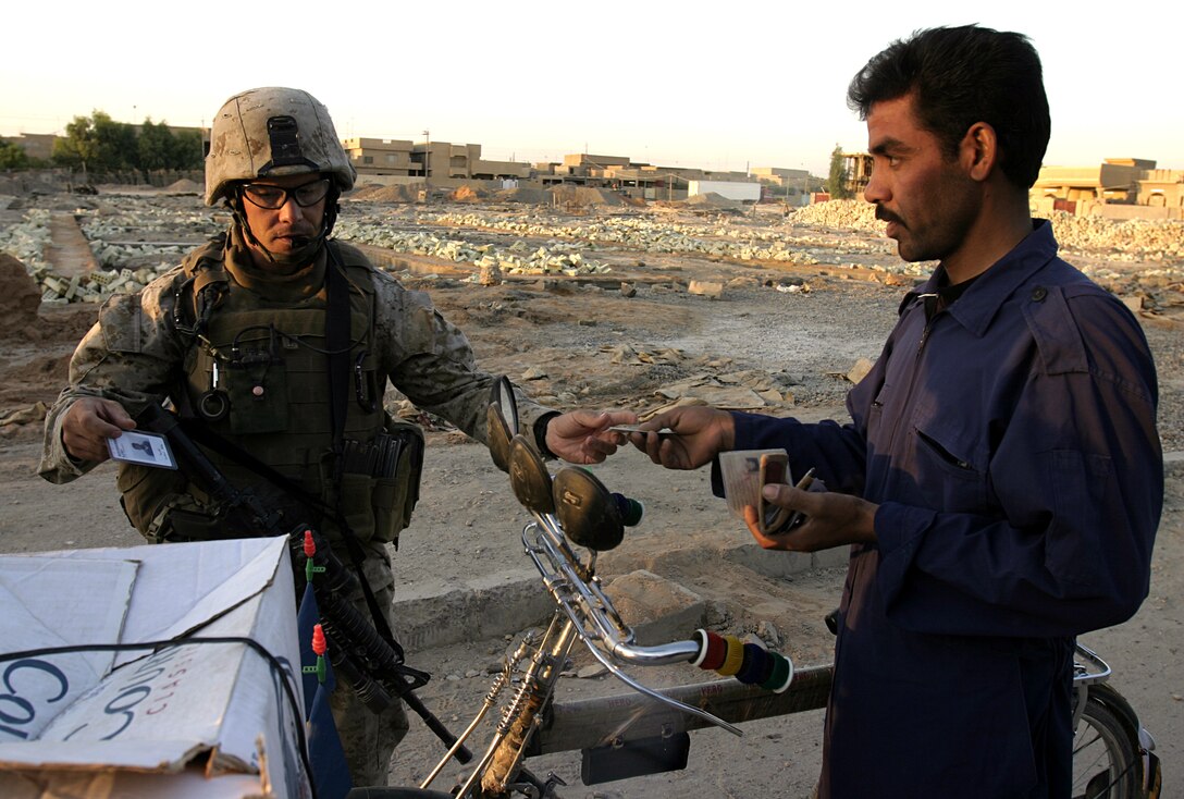 FALLUJAH, Iraq - First Lieutenant Frank Mease, 2nd Combined Anti-Armor Team's commander, Weapons Company, 1st Battalion, 6th Marine Regiment, checks a passing resident's identification card while providing security for fellow infantrymen patrolling the city streets Sept. 17.  Weapons Company personnel have been providing outer perimeter security during hundreds of patrols, raids and house-to-house search missions since arriving here in mid-March.