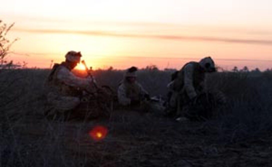 Three Marines with Bravo Co., part of Battalion Landing Team 1/1, 15th Marine Expeditionary Unit (Special Operations Capable), sit near their mortar tube as the sun rises over the horizon. The 15th MEU (SOC) is conducting security and stabilization operations in the Greater Baghdad area.