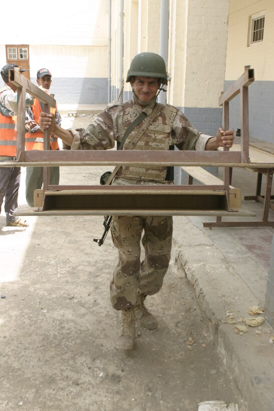 FALLUJAH, Iraq - An Iraqi soldier with the Iraqi Security Forces' 4th Company, 1st Battalion, 2nd Brigade, struggles as he carries a desk into a school here May 18.  ISF personnel worked alongside U.S. Marines to visit two local schools and distribute 59 desks.