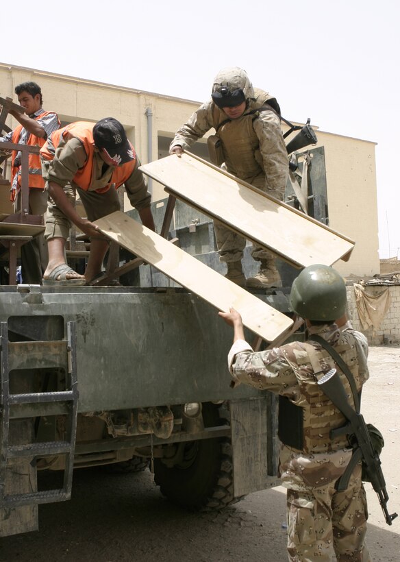 FALLUJAH, Iraq - Pfc. Carlos E. Bonano, motor transport operator with 1st Battalion, 6th Marine Regiment, helps local workers and an Iraqi soldier carry desks off a seven-ton truck and into a school here May 18.  Iraqi Security Forces worked alongside U.S. Marines to visit two local schools and distribute 59 desks.