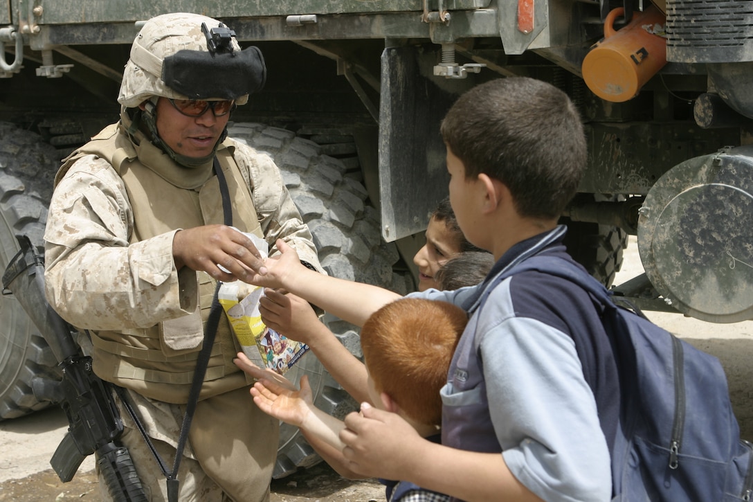 FALLUJAH, Iraq - Pfc. Carlos E. Bonano, motor transport operator with 1st Battalion, 6th Marine Regiment, provides security outside a school here May 18 as he hands Iraqi kids treats.  The 28-year-old Lancaster, Penn. native worked alongside Iraqi Security Forces to visit two local schools and distribute 59 desks.