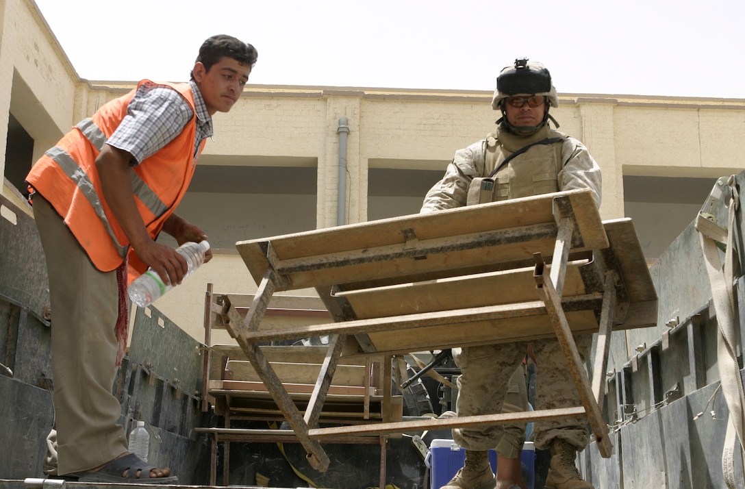 FALLUJAH, Iraq - Pfc. Carlos E. Bonano, motor transport operator with 1st Battalion, 6th Marine Regiment, helps a local worker carry desks off his seven-ton truck into a school here May 18.  The 28-year-old Lancaster, Penn. native worked alongside Iraqi Security Forces to visit two local schools and distribute 59 desks.