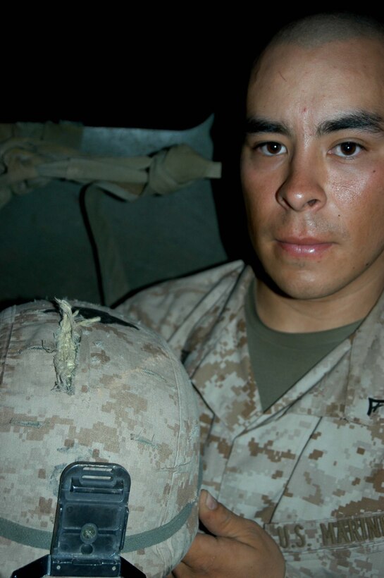 CAMP HURRICANE POINT Ar Ramadi, Iraq (June 17, 2005) - Lance Cpl. Mario R. De la Rosa, a machine gunner with 1st Squad, 3rd Platoon, Company A, 1st Battalion, 5th Marine Regiment, shows off his Kevlar helmet, which reflected an enemy sniper round and saved his life. An insurgent targeted the 20-year-old from San Francisco while he and his fellow Marines conducted a mission in the city here June 17. The 2003 Livermore High School graduate was sitting in the turret of a Humvee maning his M2.50 Caliber Machine Gun when he was shot. Photo by: Cpl. Tom Sloan