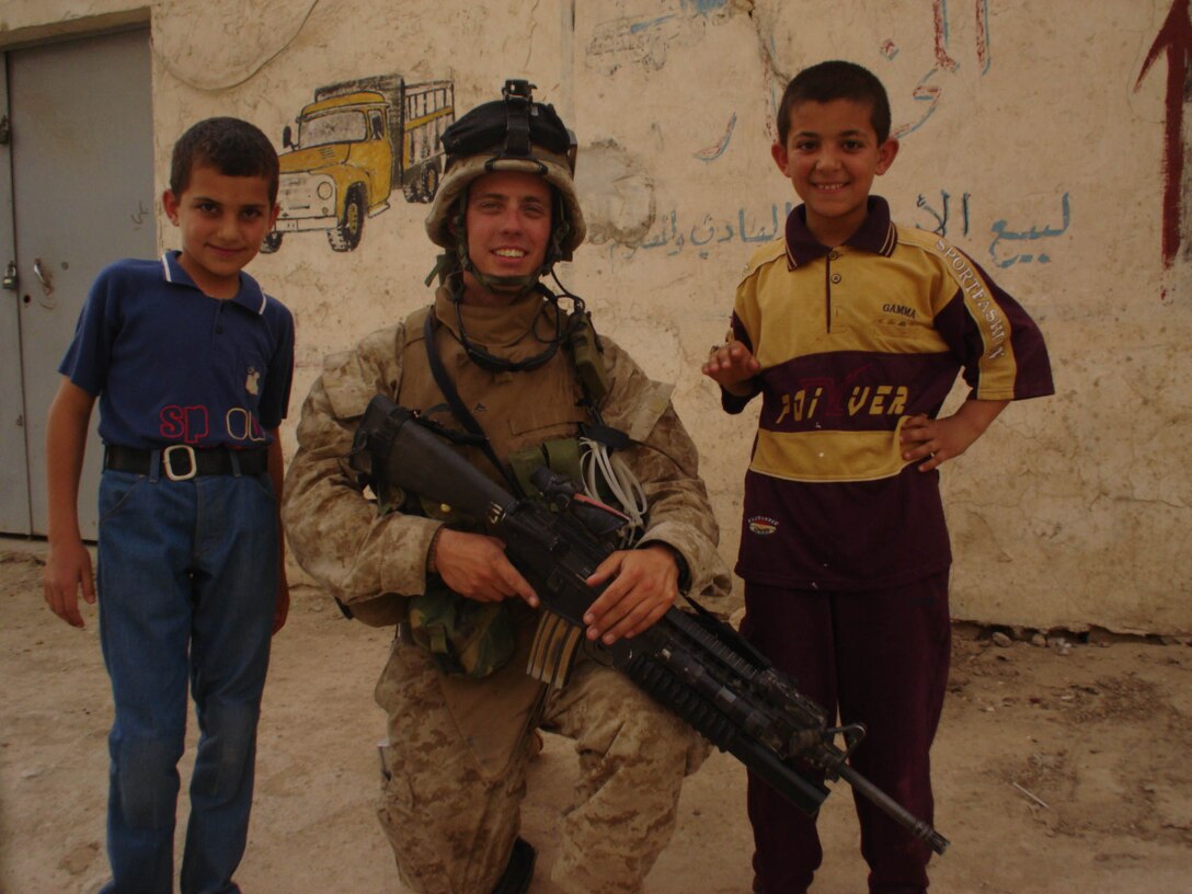 AL QA'IM, Iraq (July 16, 2005)- Lance Cpl. Benjamin D. Hallstrom, 22, a team leader with 2nd Platoon, Company K, 3rd Battalion, 2nd Marine Regiment, Regimental Combat Team-2 stops to take a photo with two Iraqi children. The Clearwater, Fla., native wants to write a book about his experiences during Operation Iraqi Freedom III to educate the American public. (Official U.S. Marine Corps photo by Lance Cpl. Lucian Friel (RELEASED)