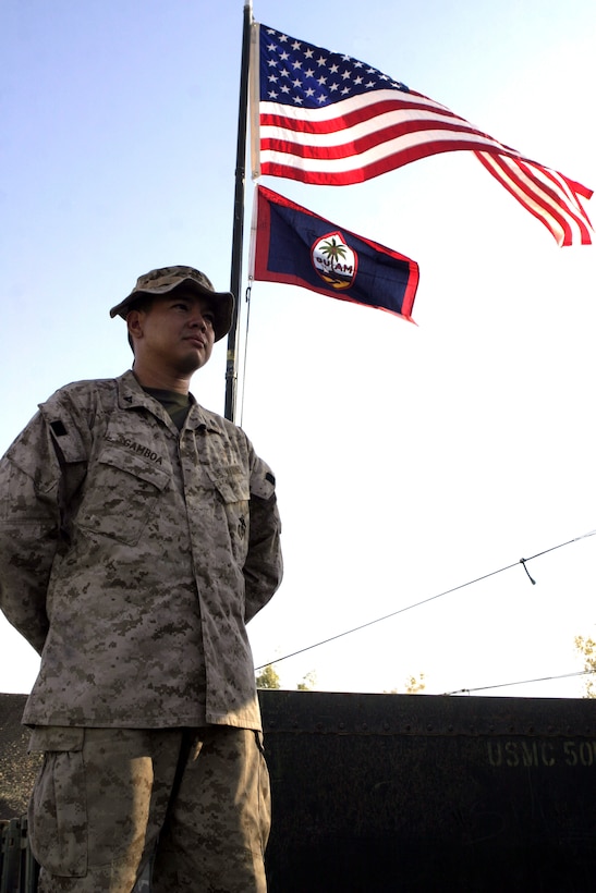 CAMP BAHARIA, Iraq - Lance Cpl. Roy L. Gamboa, a supply administration clerk with 1st Battalion, 6th Marine Regiment, stands underneath a flag pole flying his native country's and the U.S. flag.  The 28-year-old Agat, Guam native and his team of supply Marines store and keep track of millions of dollars worth of equipment their battalion's infantrymen use to conduct counterinsurgency operations in and around Fallujah.