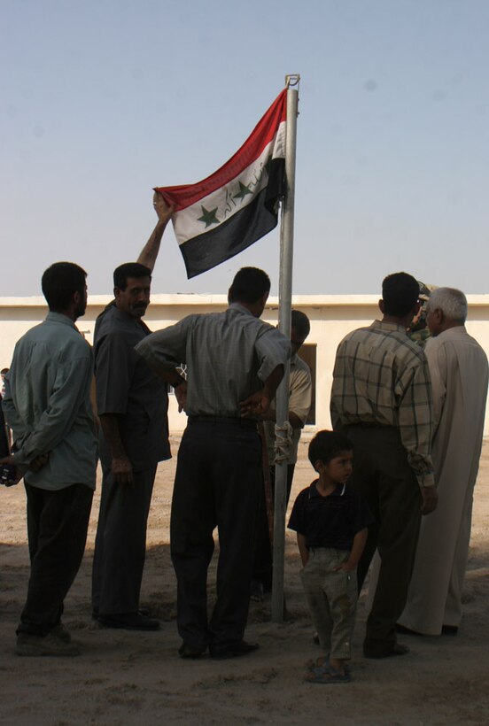 051018-M-2607O-004 KARMAH, Iraq - Teachers from the Thorouh Al Aashreen Primary School fly the Iraqi flag on a newly erected flagpole in the center of the schools courtyard before the school opening ceremony Oct. 18.  Marine from 6th Civil Affairs Group brought over 800 backpacks to hand out to students for the event.