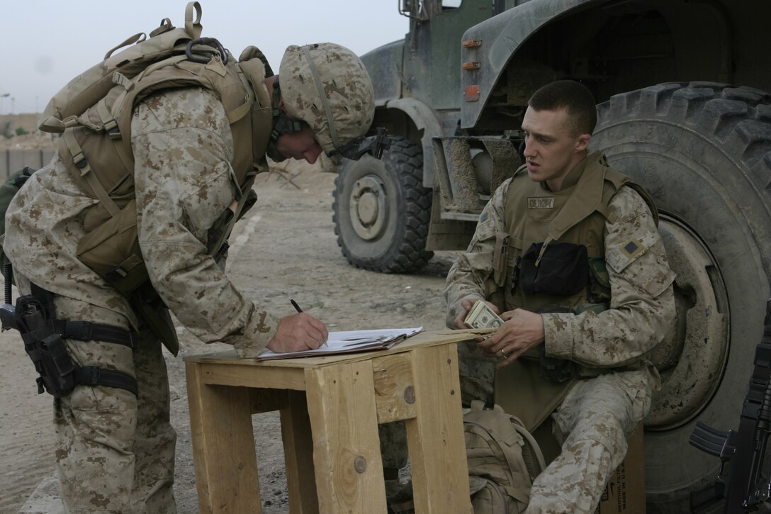 FALLUJAH, Iraq - Sgt. Jared W. Olhoft, a disbursing clerk with the 2nd Force Service Support Group, right, prepares to hand a Marine with Company B, 1st Battalion, 6th Marine Regiment money after cashing a check outside Company B's base of operations here April 19.  Olhoft offers his disbursing services as part of the 'XO's Road Show,' a Headquarters and Service Company convoy that travels once a week to the battalion's infantry companies' bases in Fallujah to offer the grunts services such as motor transport and communications equipment repair, religious services, and administrative and legal support.