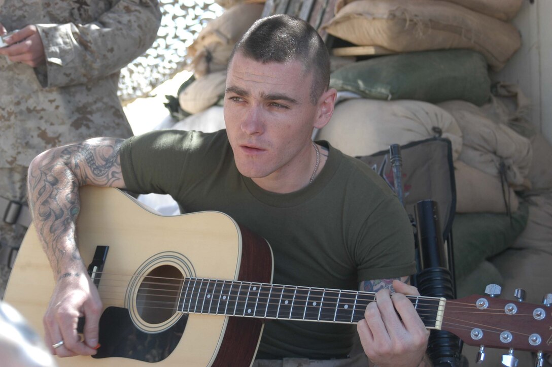 CAMP HURRICANE POINT, Ar Ramadi, Iraq (March 20, 2005) - Lance Cpl. Josh R. Barfield, assault man, 1st Platoon, 1st Squad, Company A, 1st Battalion, 5th Marine Regiment, sings while playing complementary lyrics on an acoustic guitar. The 23-year-old Glendora, Calif., native is the lead singer for up and coming metal band Blue Collar, which currently has a demo CD out. His band has also played a gig at Newport Beach, Calif. He hasn't reached international fame yet, but he has a number of fans in his unit. For the meantime, his stage is a folding chair surrounded by sandbags. He often performs for his fellow grunts here during their downtime. Photo by Cpl. Tom Sloan