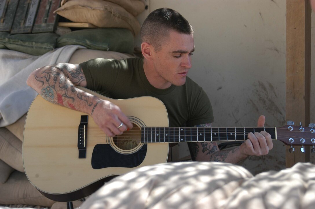 CAMP HURRICANE POINT, Ar Ramadi, Iraq (March 20, 2005) - Lance Cpl. Josh R. Barfield, assault man, 1st Platoon, 1st Squad, Company A, 1st Battalion, 5th Marine Regiment, sings while playing complementary lyrics on an acoustic guitar. The 23-year-old Glendora, Calif., native is the lead singer for up and coming metal band Blue Collar, which currently has a demo CD out. His band has also played a gig at Newport Beach, Calif. He hasn't reached international fame yet, but he has a number of fans in his unit. For the meantime, his stage is a folding chair surrounded by sandbags. He often performs for his fellow grunts here during their downtime. Photo by Cpl. Tom Sloan