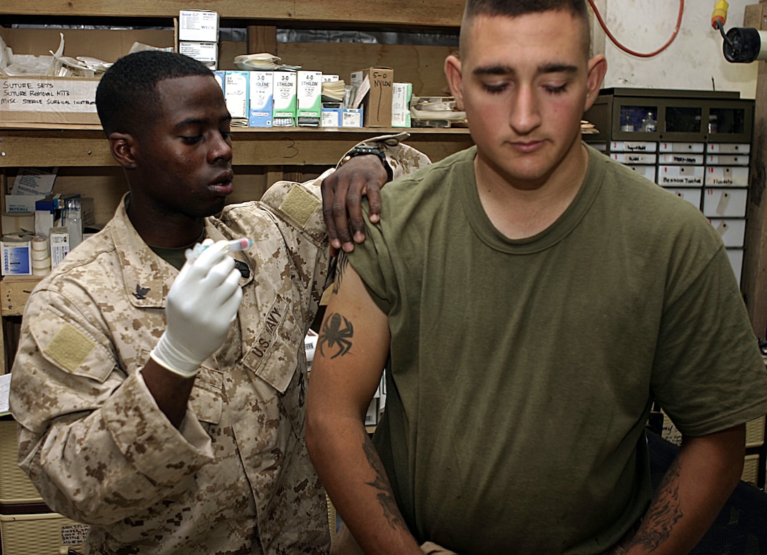 CAMP BAHARIA, Iraq - Hospitalman 3rd Class Iridious Ruise, 1st Battalion, 6th Marine Regiment's preventive medicine technician, gives a Marine a booster shot here June 7.  Ruise and fellow BAS corpsmen treat conditions such as gastrointestinal problems, insect bites, and acute illnesses.