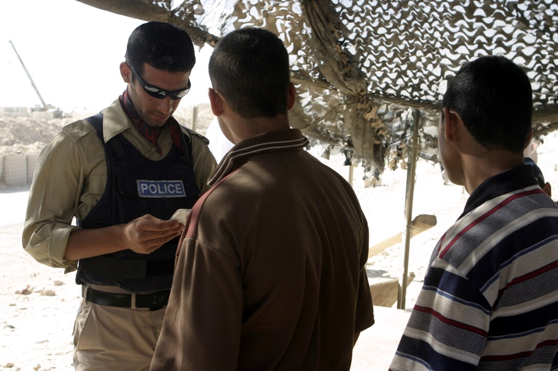 FALLUJAH, Iraq - An Iraqi policeman looks over residents' ID cards before allowing them through a check station inside northern Fallujah's Entry Control Point-2 June 10.  Iraqi Security Forces and 1st Battalion, 6th Marine Regiment personnel man this ECP and prevent weapons, explosives and insurgents from entering the city.