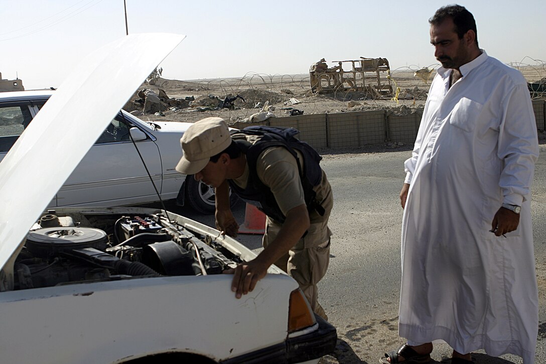 FALLUJAH, Iraq - An Iraqi policeman searches underneath a vehicle's hood in northern Fallujah's Entry Control Point-2 June 10 as the driver observes.  Iraqi Security Forces and 1st Battalion, 6th Marine Regiment personnel man this ECP and prevent weapons, explosives and insurgents from entering the city.
