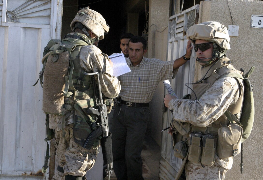 FALLUJAH, Iraq - Sergeant Thomas Sellers, 3rd squad leader, 1st Platoon, Company B, 1st Battalion, 6th Marine Regiment, right, provides security as an interpreter speaks with a man outside his residency here Aug. 20 during Operation Hard Knock.  The battalion's Marines and Iraqi Security Forces have conducted several of these operations since June to search for weapons and gather census data on the local citizens.