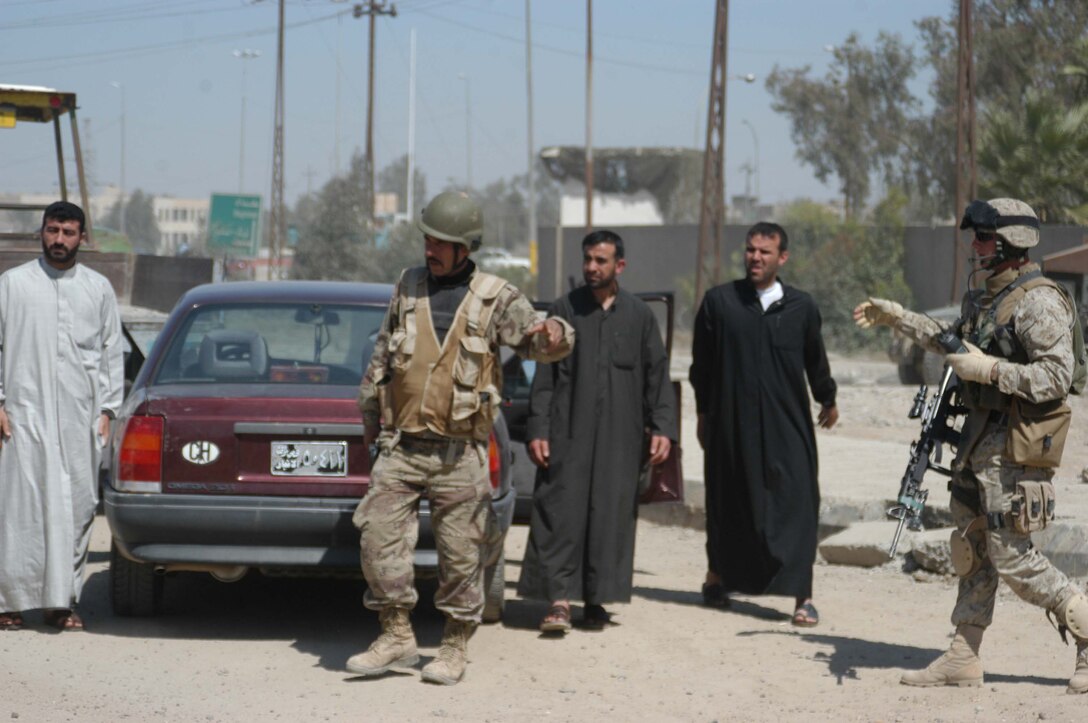 AR RAMADI, Iraq (March 21, 2005) - Captain Ada, an Iraqi Security Force Commando, instructs Iraqi's to get out of their vehicles and line up against the wall so his ISF Commandos can search their vehicles at the entry control point set up on the edge of the South Bridge here. Twenty-two-year-old Cpl. Nicholas J. Boire, squad leader, 2nd Platoon, Company C, 1st Battalion, 5th Marine Regiment, of Minnetonka, Minn., comes to his aid. Marines with Company C, 1st Battalion, 5th Marine Regiment, and ISF Commandos conduct random vehicle searches at the ECP, which is located between Marine Camps Snake Pit and Hurricane Point, around the clock in an effort to prevent explosives and weapons from being brought into the city. The Marines are currently the over watch for the ISF Commandos as they conduct the searches. Between 500 and 1000 vehicles enter the city through the ECP each day. Photo by Cpl. Tom Sloan