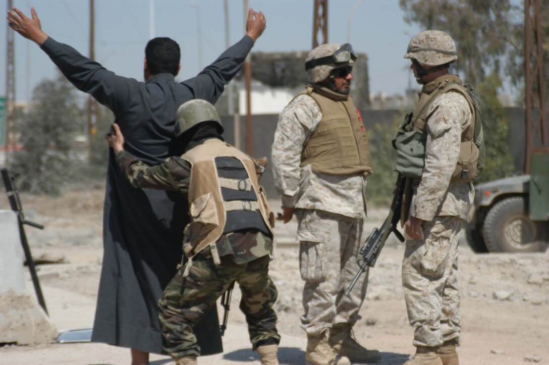 AR RAMADI, Iraq (March 21, 2005) - Fadile, an interpreter for infantry battalion, explains to 22-old Cpl. Nicholas J. Boire, squad leader, 2nd Platoon, Company C, 1st Battalion, 5th Marine Regiment, of Minnetonka, Minn., why 23-year-old Sgt. Heicen, an Iraqi Security Force Commando, is searching an Iraqi man at the entry control point set up on the edge of the South Bridge here.The search criterion for the day was farm equipment and motorcycles. Marines with Company C, 1st Battalion, 5th Marine Regiment, and ISF Commandos conduct random vehicle searches at the ECP, which is located between Marine Camps Snake Pit and Hurricane Point, around the clock in an effort to prevent explosives and weapons from being brought into the city. The Marines are currently the over watch for the ISF Commandos as they conduct the searches. Between 500 and 1000 vehicles enter the city through the ECP each day. Photo by Cpl. Tom Sloan