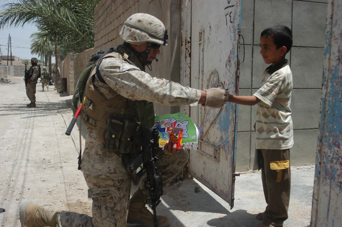 AR RAMAMDI, Iraq (May 21, 2005) - Corporal Kelly P. Baker, a team leader and rifleman with 2nd Squad, 1st Platoon, Company C, 1st Battalion, 5th Marine Regiment, gives an Iraqi boy crayons and a coloring book during a mission in the city here. The 21-year-old from New Town, N.D., and his fellow 2nd Squad leathernecks often carry candy and other gifts with them to give to Iraqi children when they patrol though their neighborhoods. Photo by: Cpl. Tom Sloan