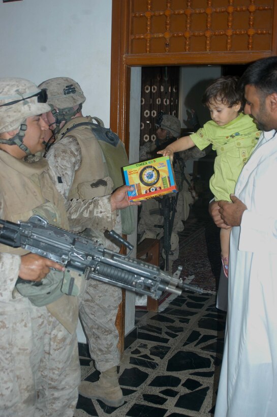 AR RAMAMDI, Iraq (May 21, 2005) - Lance Cpl. Robert P. Rodriguez, a squad automatic machine gunner with 2nd Squad, 1st Platoon, Company C, 1st Battalion, 5th Marine Regiment, gives an young Iraqi girl a Timex educational toy that teaches how to tell time and count money during a mission in the city here. The 23-year-old from Lexington, Texas, and his fellow 2nd Squad leathernecks often carry candy and other gifts with them to give to Iraqi children when they patrol though their neighborhoods. Photo by: Cpl. Tom Sloan