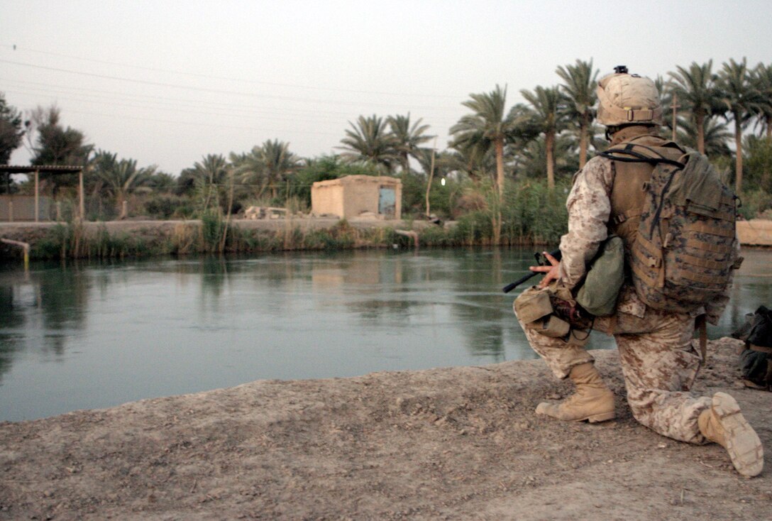 SAQLAWIYAH, Iraq - Cpl. Shane Kent, 1st Squad leader, 4th Platoon, Company A, 1st Battalion, 6th Marine Regiment, provides security along a pond in the farm fields here July 21 during Operation Hard Knock.  Company A personnel worked alongside Iraqi Security Forces to sweep through northern Saqlawiyah's Al Zakarit district to look for weapons and insurgent activity, as well as gather census information on the populace.