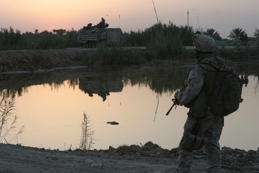 SAQLAWIYAH, Iraq - Cpl. Shane Kent, 1st Squad leader, 4th Platoon, Company A, 1st Battalion, 6th Marine Regiment, provides security along a pond in the farm fields here July 21 during Operation Hard Knock.  Company A personnel worked alongside Iraqi Security Forces to sweep through northern Saqlawiyah's Al Zakarit district to look for weapons and insurgent activity, as well as gather census information on the populace.