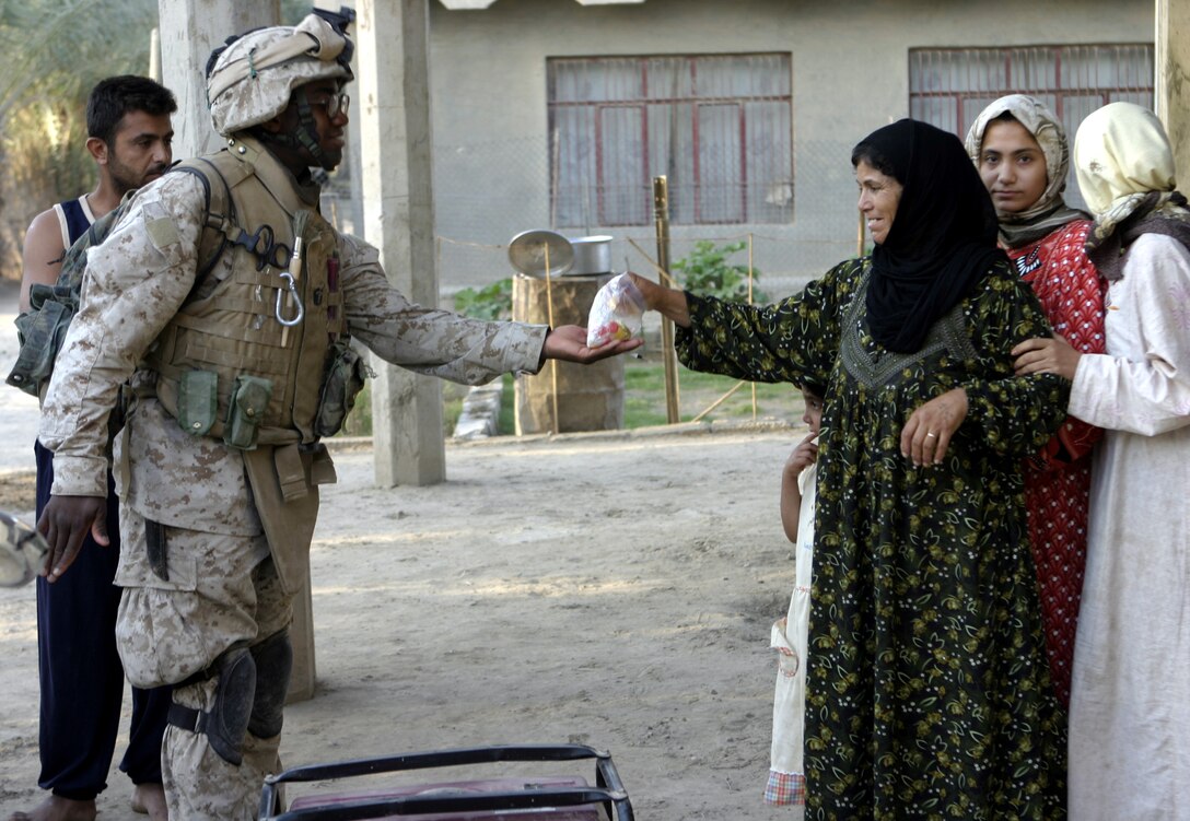 SAQLAWIYAH, Iraq - Hospitalman Clarence Washington, a corpsman with 4th Platoon, Company A, 1st Battalion, 6th Marine Regiment, hands out candy to some local women to give to their children here July 21 during Operation Hard Knock.  Company A personnel worked alongside Iraqi Security Forces to sweep through northern Saqlawiyah's Al Zakarit district to look for weapons and insurgent activity, as well as gather census information on the populace.