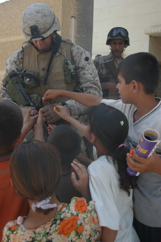 AR RAMAMDI, Iraq (May 21, 2005) - Corporal Kelly P. Baker, a team leader and rifleman with 2nd Squad, 1st Platoon, Company C, 1st Battalion, 5th Marine Regiment, gives out crayons and coloring books to a group of Iraqi children during a mission in the city here. The 21-year-old from New Town, N.D., and his fellow 2nd Squad leathernecks often carry candy and other gifts with them to give to Iraqi children when they patrol though their neighborhoods. Photo by: Cpl. Tom Sloan