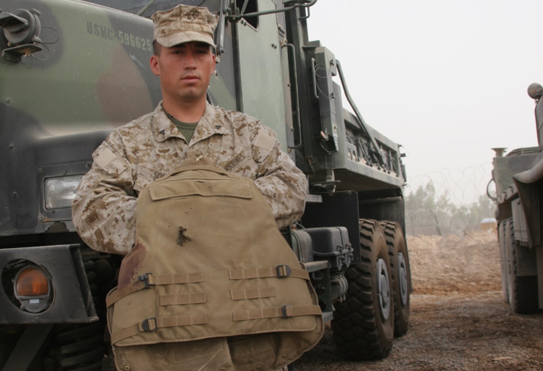 050723-M-2607O-003 CAMP FALLUJAH, Iraq -- Lance Cpl. Pascual Solis holds his flack jacket showing the damage done by shrapnel from an Improvised Explosive Device while on a Convoy back to Camp Fallujah, July 22.  The armor he wore saved him from any serious injuries to his torso or neck.
