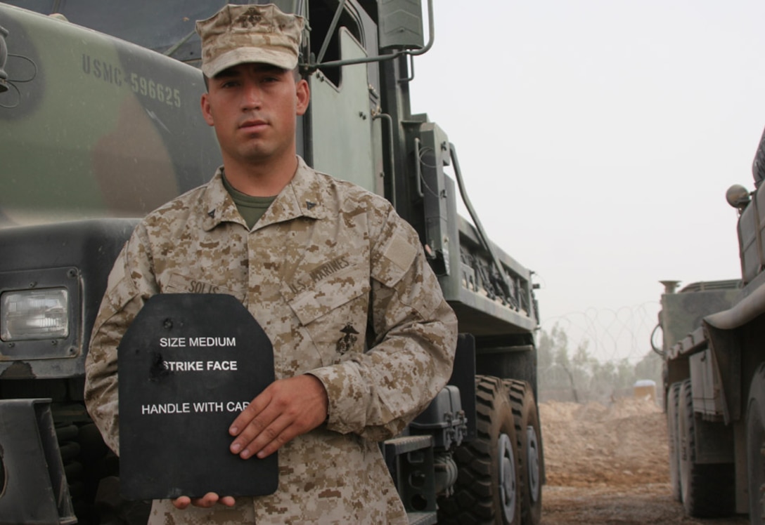 050723-M-2607O-006 CAMP FALLUJAH, Iraq -- Lance Cpl. Pascual Solis holds his armor plage showing the damage done by shrapnel from an Improvised Explosive Device while on a Convoy back to Camp Fallujah, July, 22.  The armor he wore saved him from any serious injuries to his torso or neck.