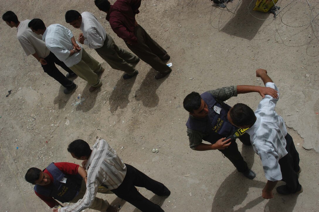 AR RAMADI, Iraq (May 24, 2005) - Two Iraqi Police Officers search men at the Ramadi Police Headquarters here. The men volunteered to be an Iraqi Police Officer and must undergo screening by 1st Battalion, 5th Marine Regiment, at their facility inside the police headquarters before being issued a sidearm, badge and paid a salary. The infantry battalion is conducting an operation to ensure qualified men fill the forces' ranks. The men take a written and oral exam, are given a physical examination, are entered into the infantry battalion's biometric automated toolset and are questioned as to why they want to serve. More than 500 Iraqis have volunteered. Photo by: Cpl. Tom Sloan