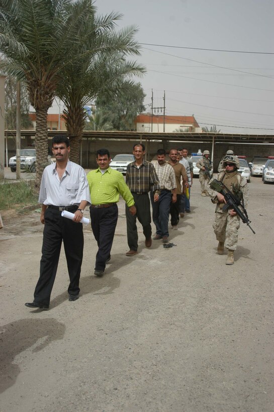 AR RAMADI, Iraq (May 24, 2005) - Lance Cpl. Christopher M. Johnson, a legal clerk with Headquarters and Service Company, 1st Battalion, 5th Marine Regiment, escorts 10 Iraqi men to a screening facility the infantry battalion has set up in the Ramadi Police Headquarters here. The men volunteered to be Iraqi Police Officers and must undergo screening before being issued a sidearm, badge and paid a salary. The infantry battalion is conducting an operation to ensure qualified men fill the forces' ranks. The men take a written and oral exam, are given a physical examination, are entered into the infantry battalion's biometric automated toolset and are questioned as to why they want to serve. More than 500 Iraqis have volunteered. Johnson, a 23-year-old from Maybee, Mich., is permanent personnel at the facility. Photo by: Cpl. Tom Sloan