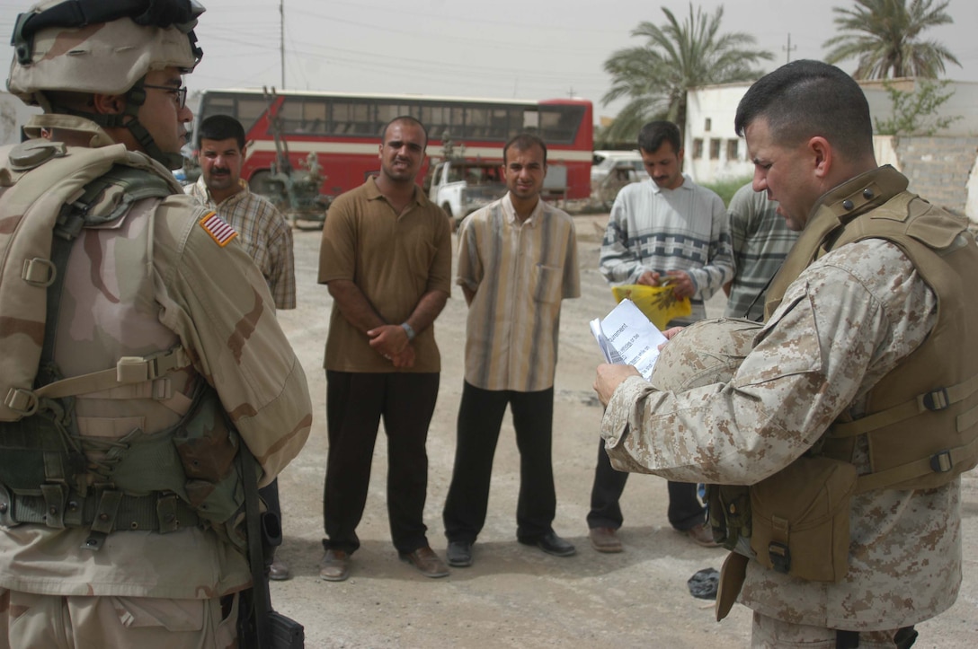 AR RAMADI, Iraq (May 24, 2005) - Captain Barton K. Nagle, the intelligence officer for Headquarters and Service Company, 1st Battalion, 5th Marine Regiment, relays a brief to the Iraqis through Spc. Redouane Rahli, a linguist with 2nd Brigade Combat Team, at the Ramadi Police Headquarters. The men volunteered to be an Iraqi Police Officer and must undergo screening at 1st Battalion, 5th Marines' facility before being issued a sidearm, badge and paid a salary. The infantry battalion is conducting an operation to ensure qualified men fill the forces' ranks. The men take a written and oral exam, are given a physical examination, are entered into the infantry battalion's biometric automated toolset and are questioned as to why they want to serve. More than 500 Iraqis have volunteered. Photo by: Cpl. Tom Sloan