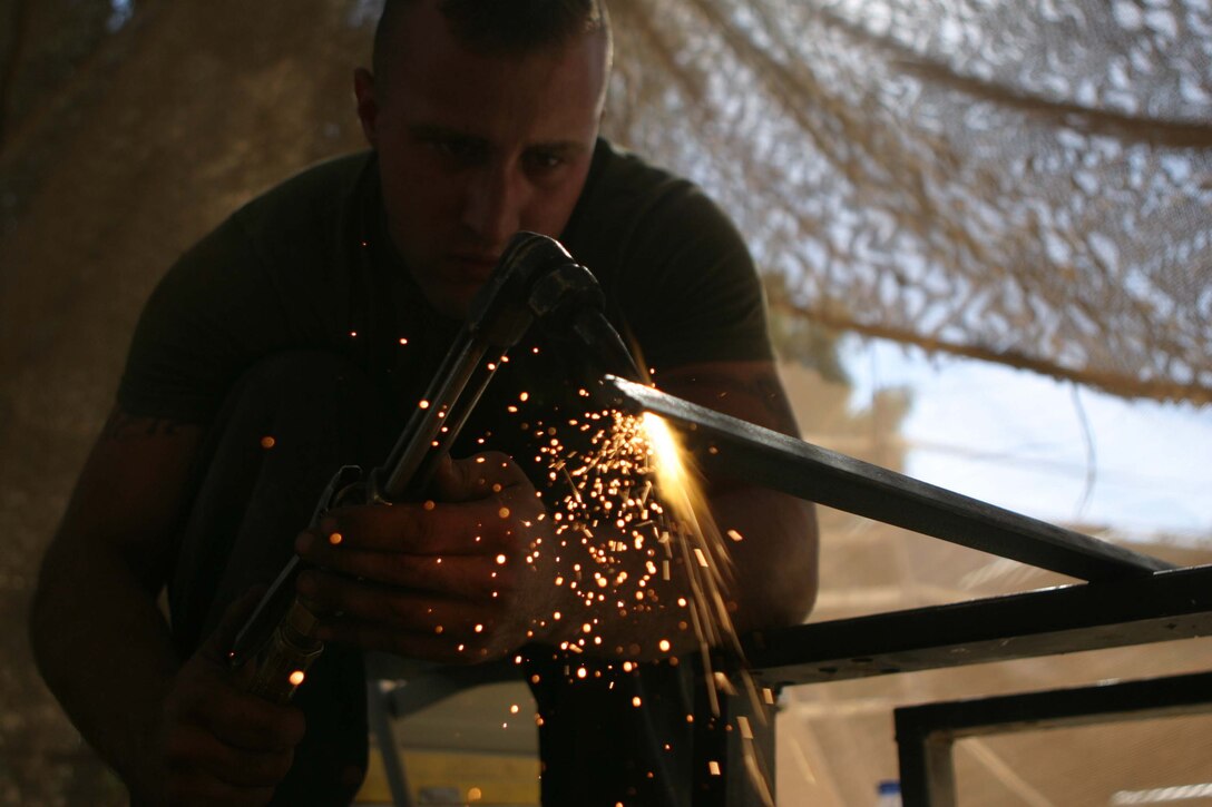 CAMP BLUE DIAMOND, RAMADI, Iraq - Lance Cpl. Anthony S. Loftin a motor transport mechanic with Truck Company, Headquarters Battalion, 2nd Marine Division  cuts a piece of metal with an acetylene torch to be welded into a gate that will be used to help lead Iraqi citizens into the Al Anbar Government Center to vote in Iraq's elections this October. Loftin has used the welding skills he learned while working at his grandfathers automotive shop in Arkansas to fabricate the numerous guard towers, rolling gates and other metal structures on the camp. Official Marine Corps photo by: Sgt Ryan S. Scranton