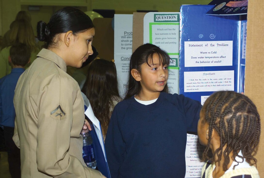 Lance Cpl. Johanna Herrera, disbursing clerk for the Finance Office, judges Yessenia's, 9, progect on how water temperature affects the behavior of snails during the District Science Fair held at Barstow Community College Thursday.
