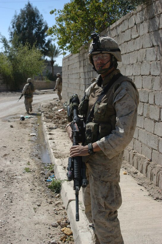 AR RAMADI, Iraq (March 25, 2005) - Twenty-two-year-old Johnny L. Alvarez, rifleman, 1st Squad, 1st Platoon, Company B, 1st Battalion, 5th Marines, of Garden Grove, Calif., turns to look behind him while patrolling a road with his squad. Leathernecks with 1st Platoon, Company B, 1st Battalion, 5th Marines, searched several houses in the western part of the city here March 25 for a man they suspect is a member of the jihad group Jaysh Mohamed, which is connected with producing improvised explosive devises and has been linked to several IED attacks. They also searched for illegal weapons, weapons caches and checked identification cards of the men in each house they searched. The Marines were accepted well by the people they searched and by the children who gathered around them in the streets. The Marines gave out soccer balls, pens and paper, sunglasses and candy to the children. Photo by Cpl. Tom Sloan