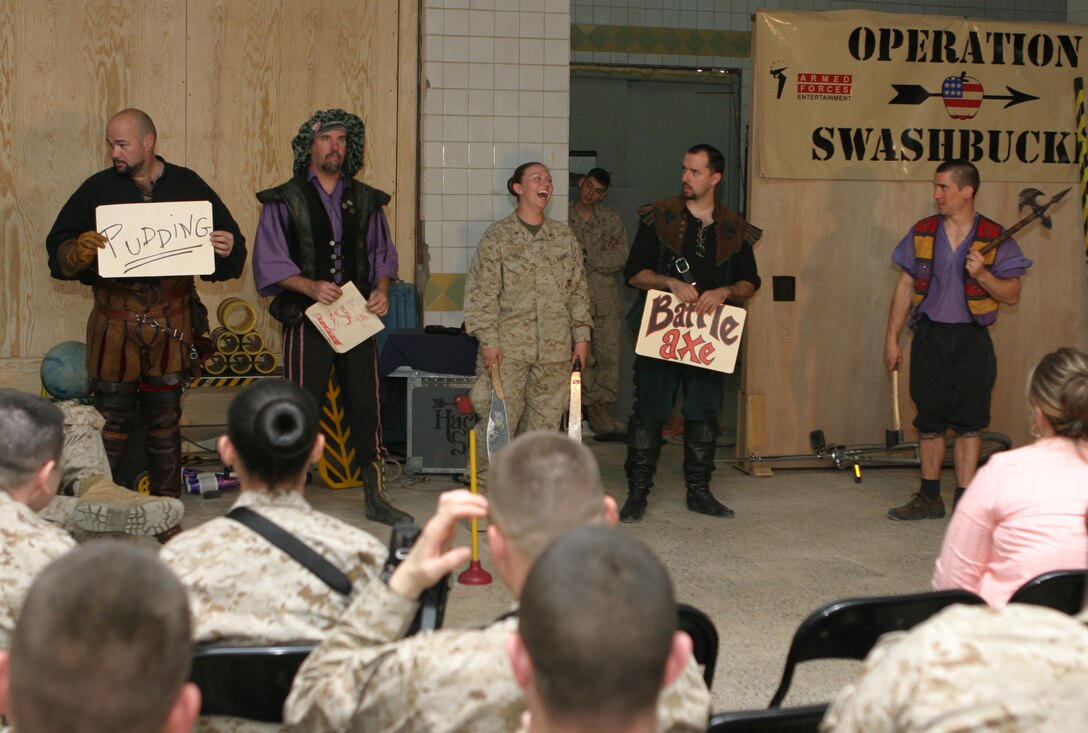 CAMP BLUE DIAMOND, AR RAMADI, Iraq - Lance Cpl. Holly Charette, a 21-year-old mail clerk from Cranston, R.I. laughs as "Hack" John Davis holds up a sign a sign for pudding as one of the choice for Juggler, comedian and award-winning motivational speaker, Dan Thurmon, to juggle during Operation Swashbuckle. Thurmon is a member of the four-man comedy show presented by Hack and Slash, who provided an explosive round of entertainment for more than 100 Marines, sailors and soldiers here serving with the 2nd Marine Division in support of Operation Iraqi Freedom.