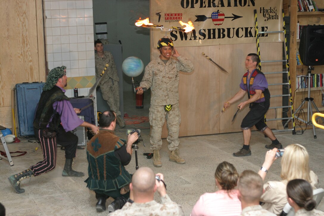 CAMP BLUE DIAMOND, AR RAMADI, Iraq - Corporal Vladimir J. Espinal, a 22-year-old member of the camp's quick reaction force and New York native, displays his confidence in the abilities of the juggling comic team, Dan Thurmon (right) and Todd Key  (left) during Operation Swashbuckle. Espinal is equipped with a flaming propeller upon his head and holding a spinning ball on a drill while the two comedians juggle knives to his front and back. This was part of a four-man comedy show presented by Hack and Slash, who provided an explosive round of entertainment for more than 100 Marines, sailors and soldiers here serving with the 2nd Marine Division in support of Operation Iraqi Freedom.