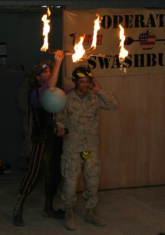 CAMP BLUE DIAMOND, AR RAMADI, Iraq - Corporal Vladimir J. Espinal, a 22-year-old member of the camp's quick reaction force and New York native, is geared up to assist the juggling comic team, Dan Thurmon (right) and Todd Key  (left) during Operation Swashbuckle. The team is part of a four-man comedy show presented by Hack and Slash, who provided an explosive round of entertainment for more than 100 Marines, sailors and soldiers here serving with the 2nd Marine Division in support of Operation Iraqi Freedom.